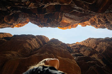 Woman looking up through steep canyon walls to blue sky