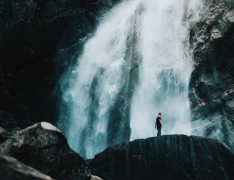 person standing on rocks in front of huge waterfall