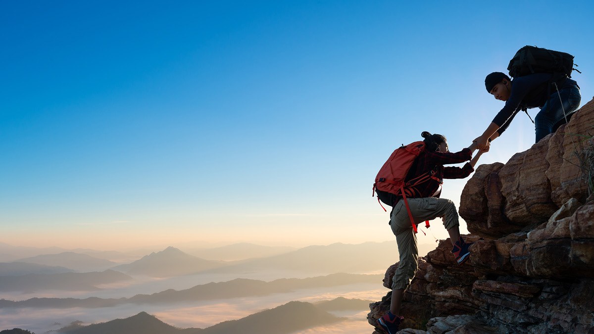 two backpackers, one is helping another climb atop a rock